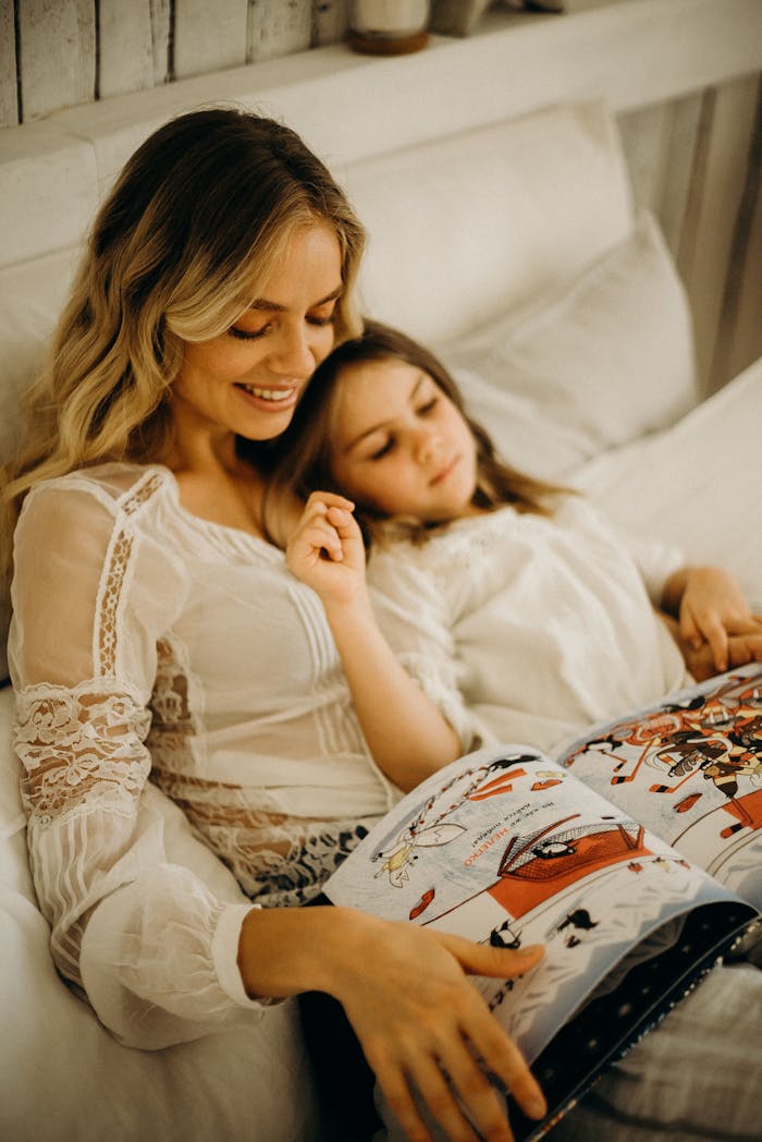 A mother and daughter enjoy a cozy moment reading together in a comfortable bedroom setting.