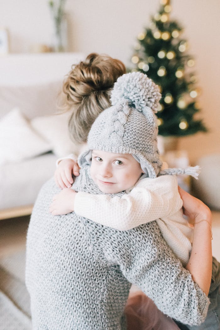 A mother and child sharing a warm embrace wearing cozy knitwear in a cozy home setting.